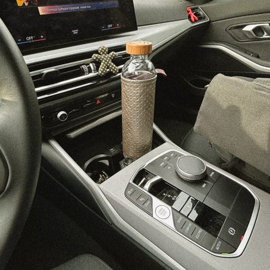 Botella de vidrio con funda texturizada y tapón de madera para la hidratación, en el posavasos de un coche.