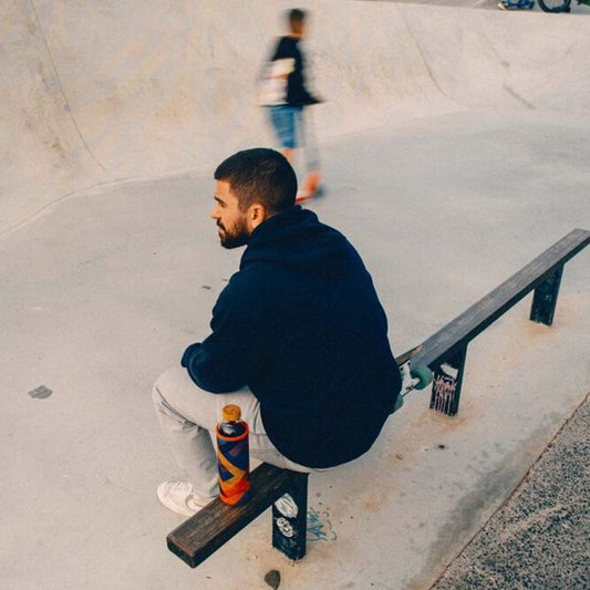 Hombre descansando en un skatepark, con su botella para la hidratación sobre una barandilla a su lado.