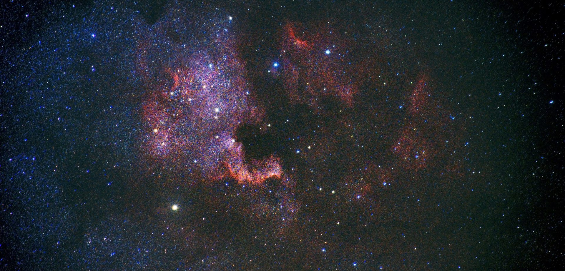 Cielo nocturno vívido que muestra una galaxia colorida con estrellas brillantes y tenues dispersas sobre un fondo oscuro.