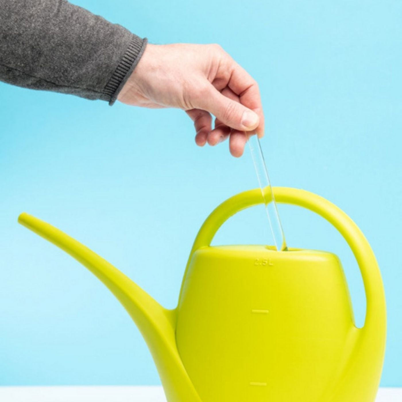 flaska green varilla de vidrio programado para estructurar el agua de tus plantas, una mano esta insertando la varilla en una regadera de color verde fluor sobre fondo azul